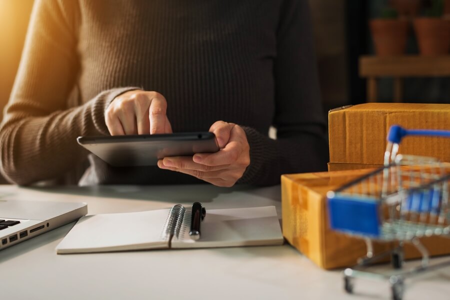 Caso de éxito Mundo Fit - Online seller managing ecommerce orders with a tablet and shipping boxes.